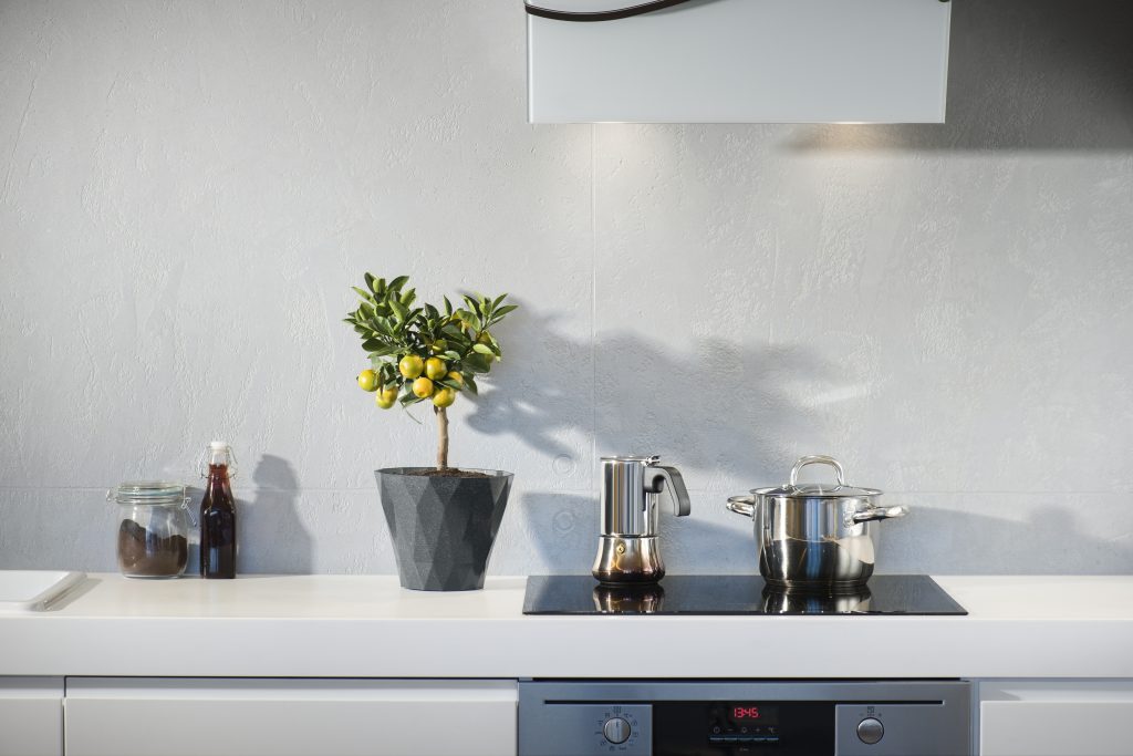 Modern kitchen with a small lemon tree, stovetop espresso maker, and cooking pot on a white countertop.