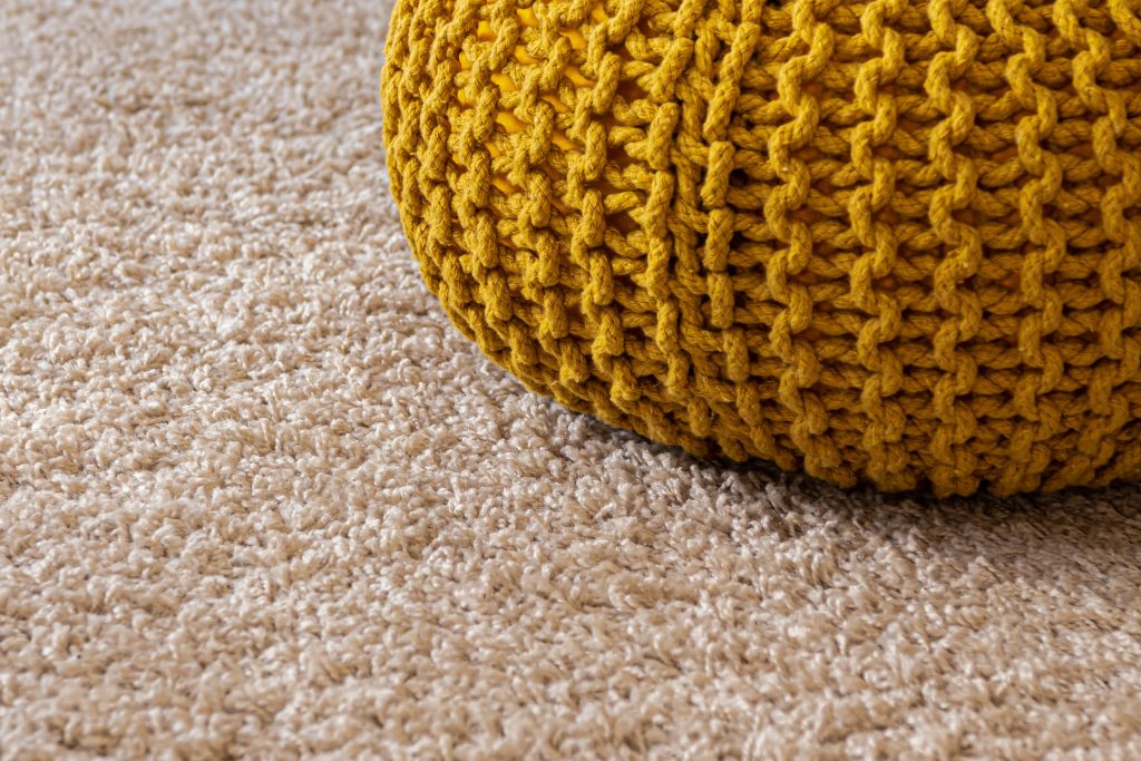 Close-up of a beige carpet with a yellow knitted pouf on top