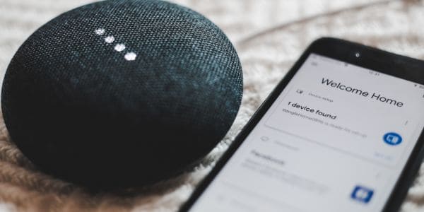 A black Google Home next to a smart phone 