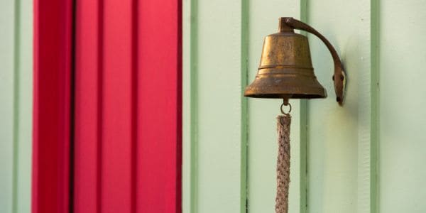 A bell mounted on a read and green cladding wall 
