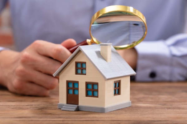 Hand holding magnifying glass looking at a miniature home 