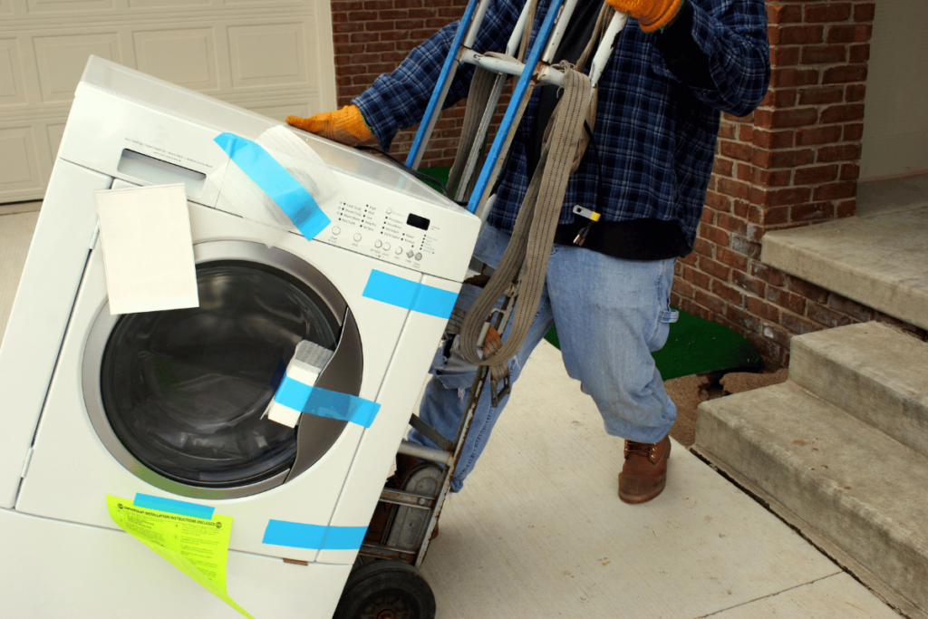a removalist moving a washing machine. the removalist uses a trolley, a moving belt and has the laundry machine taped up
