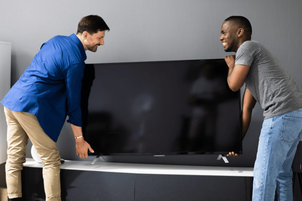 Two men placing a big TV on a white table 