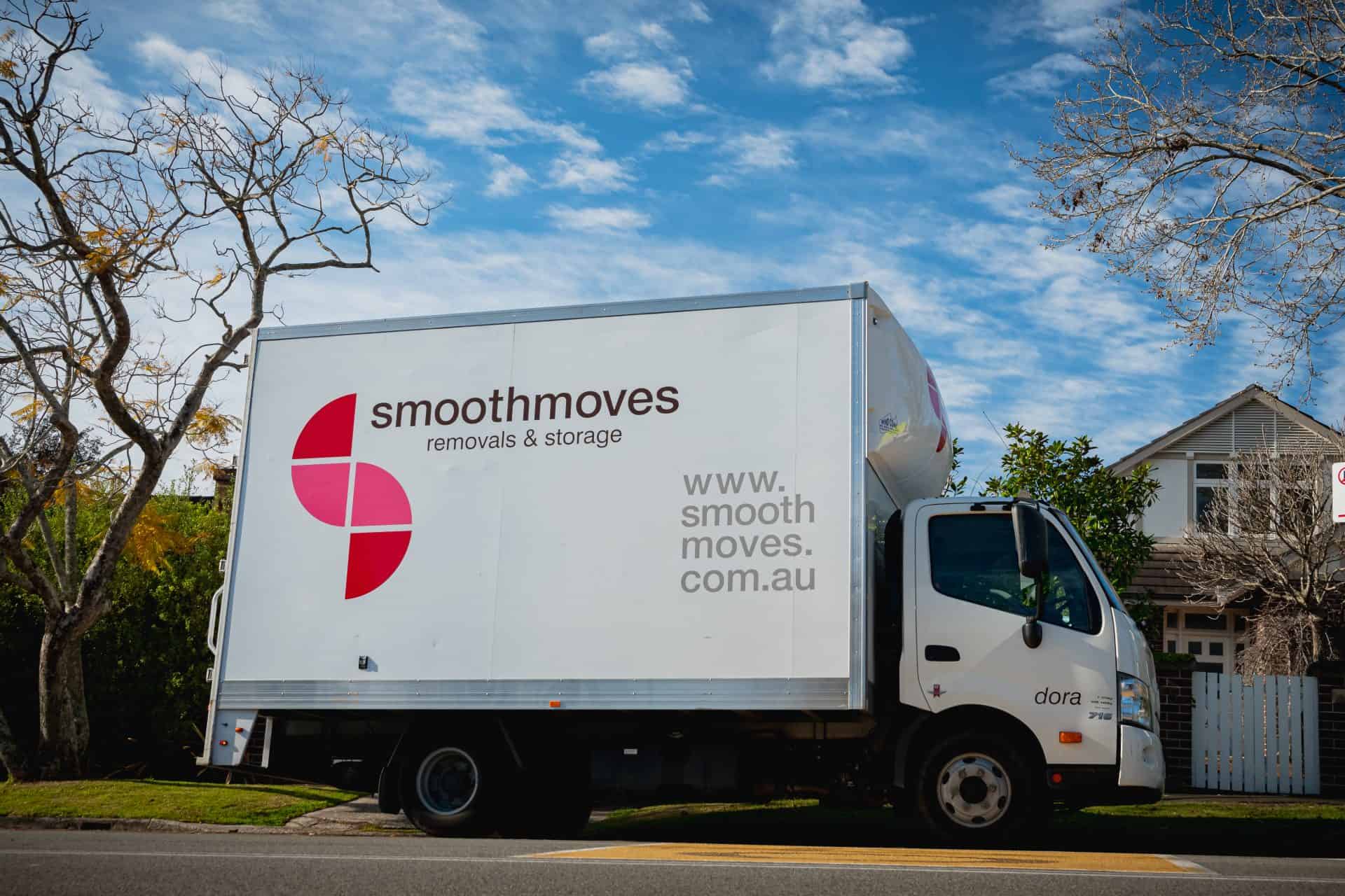 A white Smoothmoves removals and storage truck parked on a tree-lined street